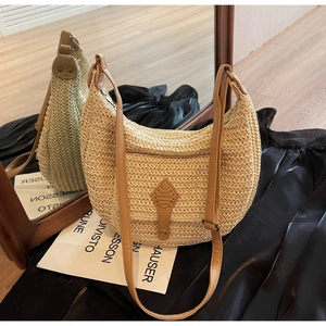 Close-up of a woven straw hobo bag with brown leather strap and diamond patch detail