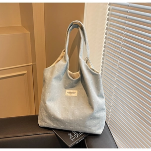 Detail of light blue denim tote bag with white heart patterns and woven label