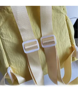 Detail of adjustable thick cream straps and white buckles on a yellow canvas backpack