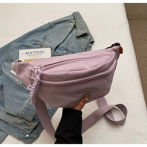 Detail of lavender canvas chest bag with dual zippers and adjustable strap on fabric