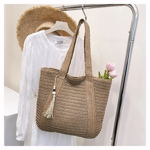Detail of straw woven tote bag with fringe charm and tulips hanging on a metal rack