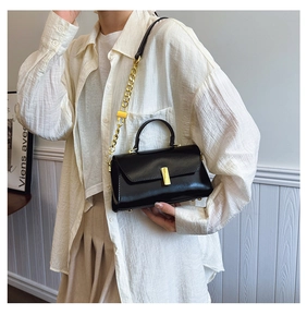 Detail of black leather crossbody bag with gold chain strap and metallic lock on model