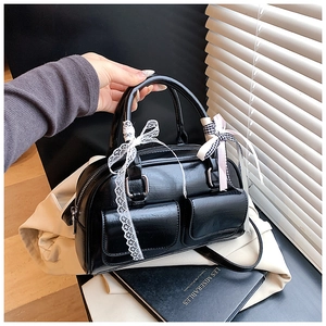 Detail of black glossy Boston bag with lace bow, ribbon charm and dual front pockets
