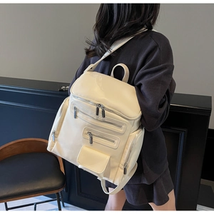 Detail view of cream-white leather backpack with multi-pocket design and utility zippers