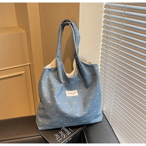 Detail of denim blue tote bag with white bow prints and rectangular brand label