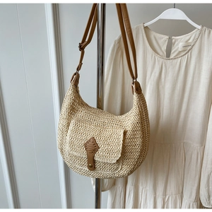 Detailed straw weave texture of a beige crescent bag with adjustable brown leather strap