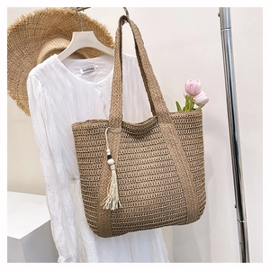 Detail of hand-woven straw tote bag featuring white fringe and wooden bead tassel accessory