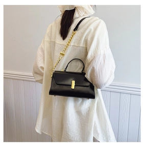 Detail view of a black leather crossbody bag with a gold metal buckle on a female model