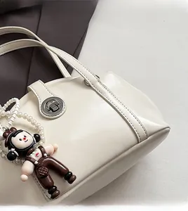 Détail du sac à main en cuir PU crème avec fermoir rotatif en métal et breloque poupée