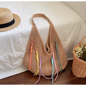 Detail of hand-woven mesh shoulder bag with colorful crochet tassels on wooden floor