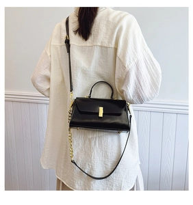 Detail of black leather crossbody bag featuring gold hardware and elegant metal chain strap