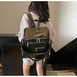 Detail of a black leather backpack with four silver zippers worn by a female model