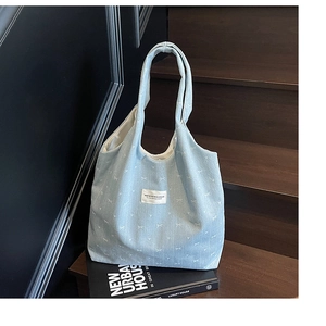 Light blue denim tote bag with white bow pattern placed on a rustic wooden staircase