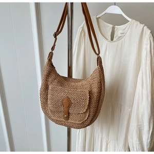 Detail of light brown straw half-moon bag with front leather flap pocket and adjustable strap