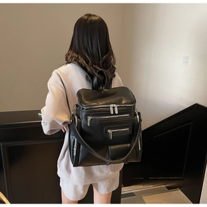 Detail of black leather backpack featuring multiple silver metal zippers and wide straps