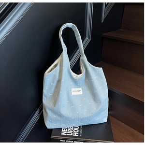 Detail of light blue denim tote bag with white bow patterns and rectangular brand label