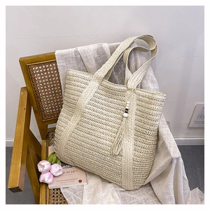 Detail of hand-woven straw tote bag with beaded tassel charm on a vintage chair