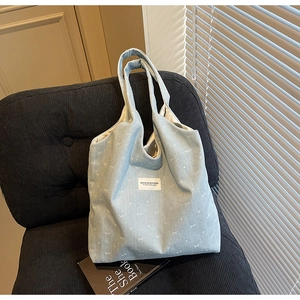 Detail of light blue denim tote bag with white bow patterns and branded woven label