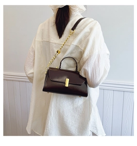Detail of dark brown polished leather square bag with vintage gold clasp and chain strap
