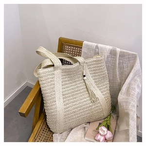 Detail of a beige woven straw tote bag with a tassel charm placed on a rattan chair