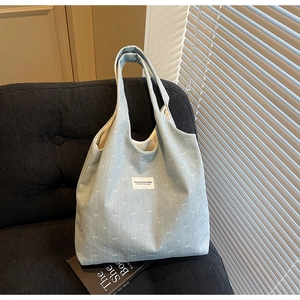 Detailed texture of light blue corduroy tote bag with white bow patterns and fabric label