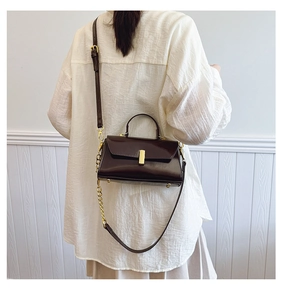 Detail of dark brown leather handbag featuring gold metal clasp and chain strap on a model