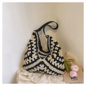 Detail of hand-woven straw tote bag in black and beige geometric pattern and leather strap