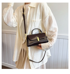 Detail of dark brown leather crossbody bag with gold chain strap worn by a model