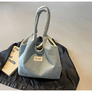 Detail of light blue corduroy tote bag with white floral bow prints on a leather jacket