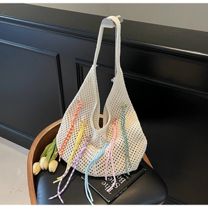 Detail of hollow-out knit tote bag featuring colorful tassels for beach vacations