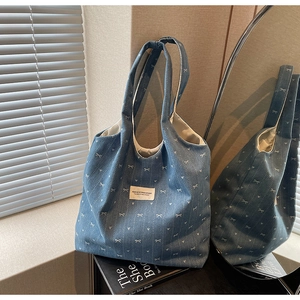 Detail of denim tote bag with white knitted bows, heart patterns and brand label