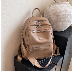 Detailed view of khaki pebbled leather backpack with silver zippers and multi-pocket design