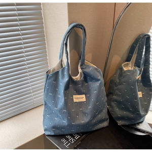 Detailed view of blue denim tote bag featuring white bow embroidery and brand label