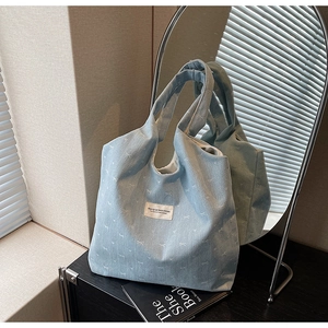 Detail of light blue denim tote bag featuring white bow embroidery and rectangular fabric label