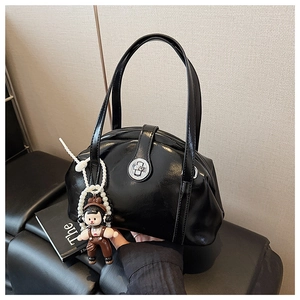 Détail d'un sac à main noir brillant avec fermoir métal et breloque peluche avec perles