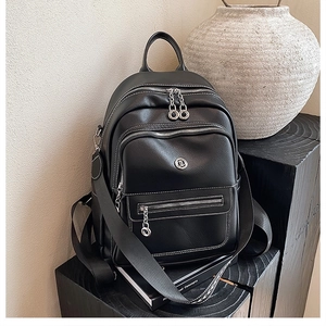 Detail of black leather backpack featuring contrast white stitching and metal logo on the base