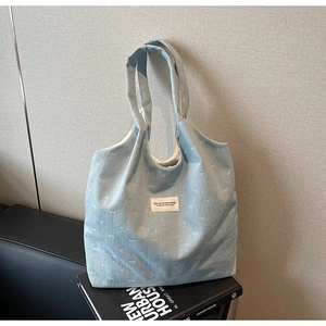 Detail of light blue denim tote bag with white bow patterns and branded patch on sofa