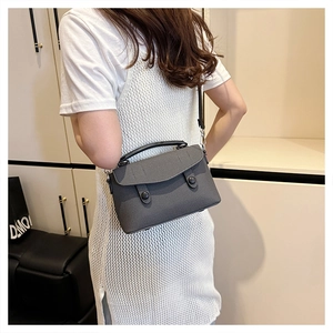 Gray crossbody bag with woven texture and black leather handle shown on model in home setting