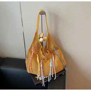 Detail of yellow hollow knit tote bag with colorful bohemian spiral tassels on black stand