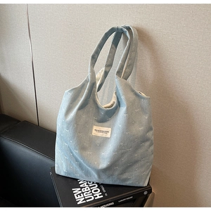 Close-up of light blue denim tote with white bow patterns and fabric label detail
