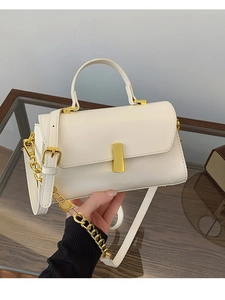 Cream square handbag with gold buckle and chain strap shown in a hand-held minimalist setting