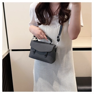 Detail of dark grey textured small square handbag with dual round buttons and top handle