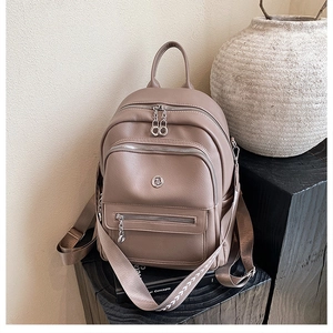 Detail of tan pebble leather backpack showing multiple zipper pockets and wide straps