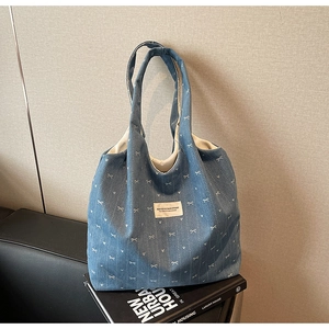 Detail view of blue denim tote bag featuring white bow prints and a soft fabric texture