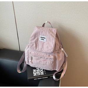 Dettaglio dello zaino in nylon rosa chiaro con logo patch su un divano nero