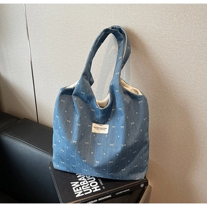 Detail of blue denim tote bag with white bow prints and brand patch on a leather sofa