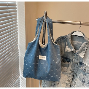 Detail of denim tote bag featuring white bow patterns and brand label on a metal hanger