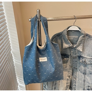 Detail of blue denim tote bag with white bow prints and brand label on a metal hanger