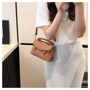Brown textured small square bag shown as a crossbody on a model with white lace outfit