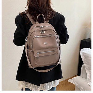 Model wearing a large khaki leather backpack with multiple zipper pockets on back